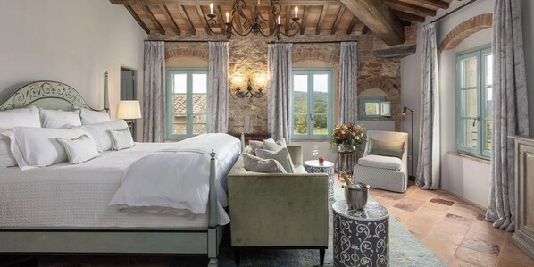 Ein Schlafzimmer mit einem großen Bett, einer Sitzecke mit einem Sessel und einem kleinen Tisch, einer Chandelüster und einer Steinwand.