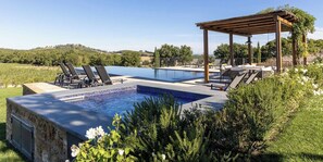 Ein Swimmingpool mit Liegestühlen und einer Pergola, umgeben von Grünflächen und Hügeln.