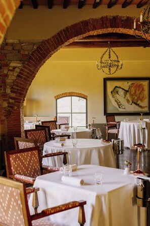 Ein Restaurant mit Backsteinbögen, weißen Tischdecken und gemusterten Stühlen.
