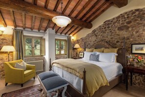 Ein Schlafzimmer mit einer Steinsäule, einer Holzbalkendecke, einem Bett mit Kopfteil, einer Bank, einem Stuhl und einem Heizkörper.