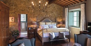 Ein Schlafzimmer mit Steinwand, einem Bett mit vielen Kissen, einem Nachttisch, einem Sessel und einem Fernseher.