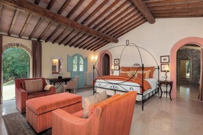 Ein Schlafzimmer mit Himmelbett, einer Sitzecke mit Sofa und Sesseln sowie Blick durch ein Rundbogenfenster.