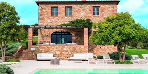 Ein Steinhaus mit Pool, Sitzgelegenheiten im Freien und einem gepflegten Garten.