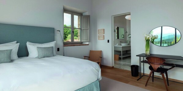 Ein Schlafzimmer mit einem Bett, einem Schreibtisch, einem Stuhl, einem Fenster und einem durch eine offene Tür einsehbaren Badezimmer.
