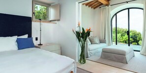 Ein Schlafzimmer mit Bett, Nachttisch, Lampe und Blick ins Freie durch ein großes Fenster.