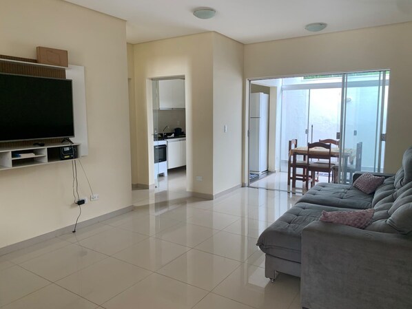 A living room with a flat-screen TV, a sofa, and a dining area with chairs.