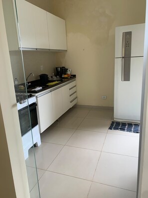 A kitchen with white cabinets, a stainless steel refrigerator, and a tiled floor. - Comfortable townhouse (Campo Grande)