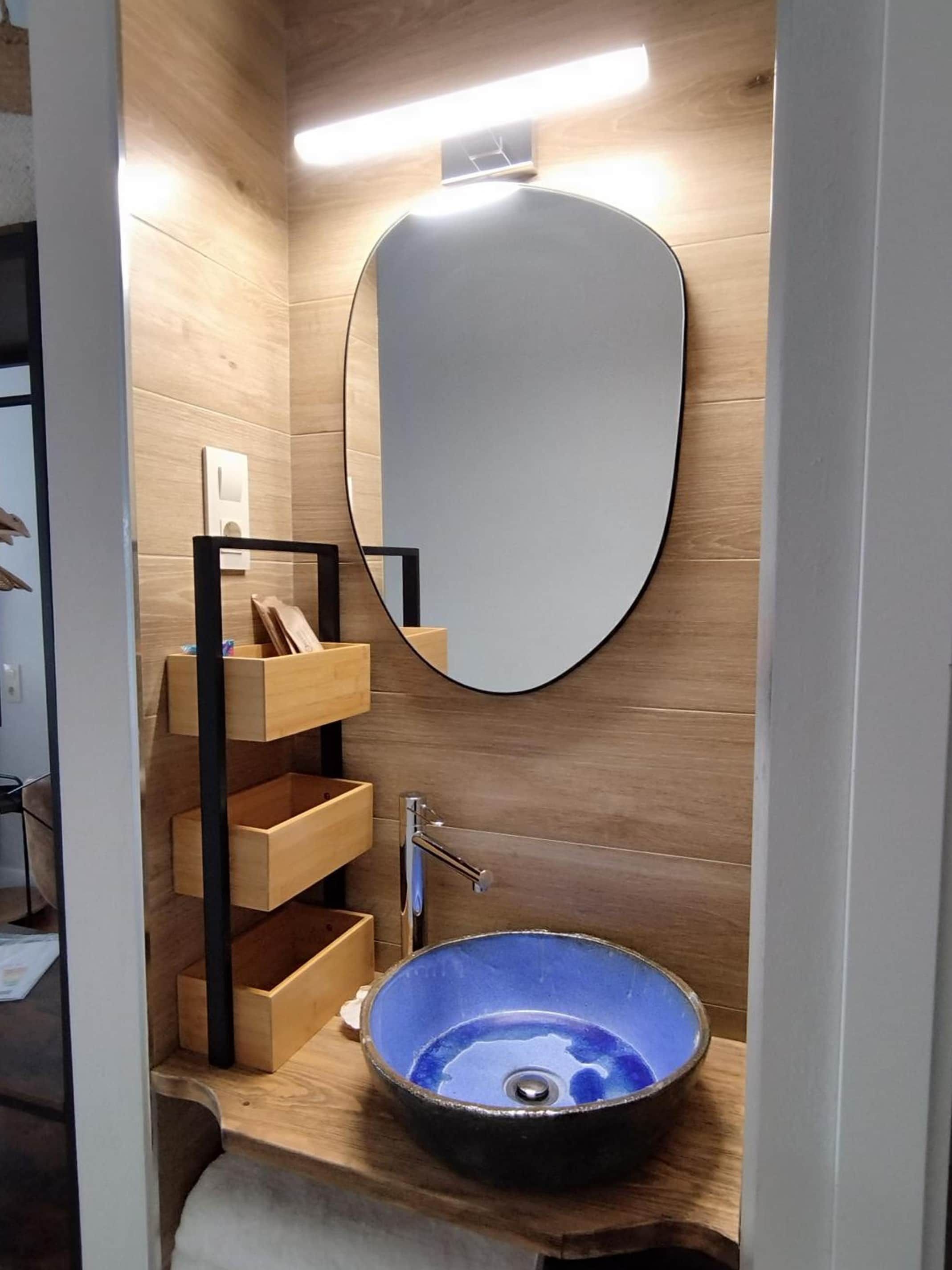 Un baño pequeño con tocador de madera, espejo redondo y lavamanos azul.
