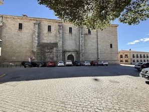 A historic stone building with a central entrance, parked cars, and a cobblestone street.