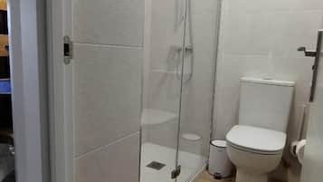 Un baño con cabina de ducha de vidrio, inodoro y lavamanos blanco.