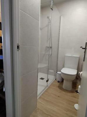 Un baño con cabina de ducha de vidrio, inodoro y lavamanos blanco.