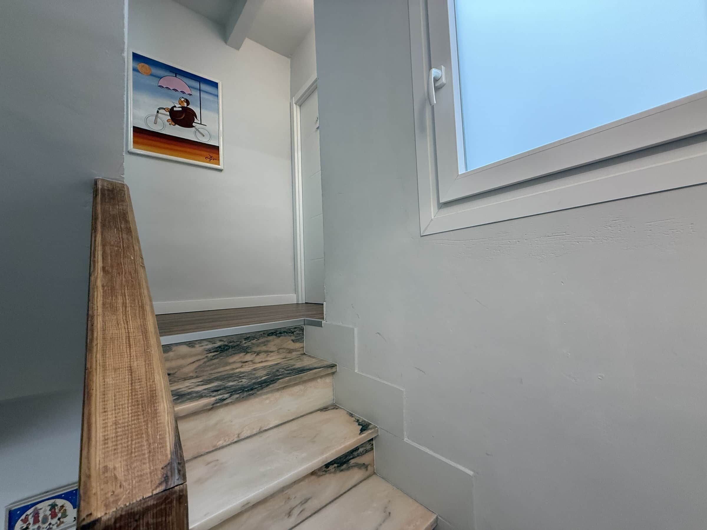 Una escalera con barandilla de madera, una ventana y un cuadro colgado en la pared.