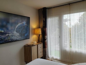Habitación de hotel con cama, mesita de noche con lámpara, un cuadro en la pared y ventana con cortinas translúcidas.