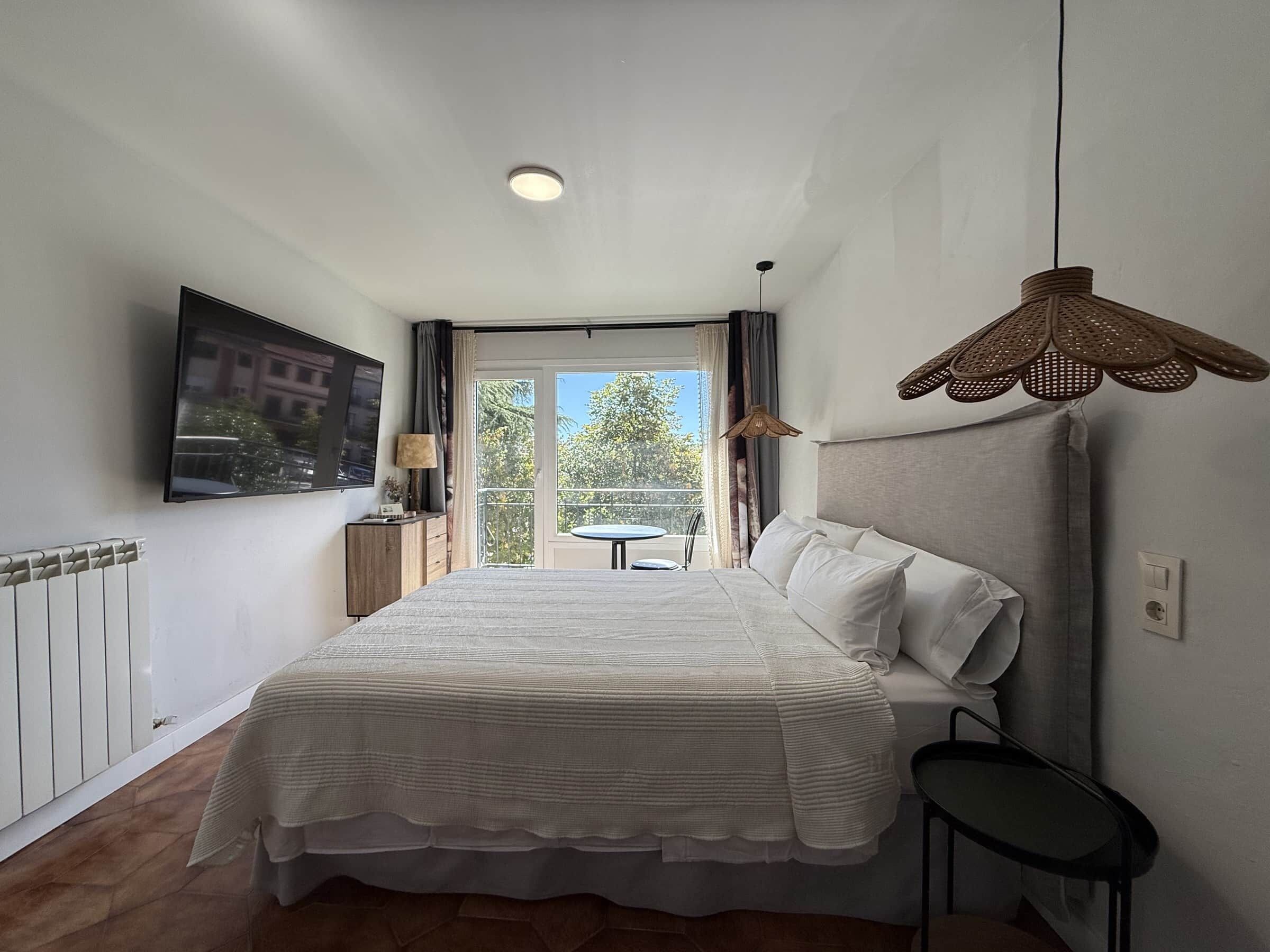 Habitación de hotel con cama, televisión, una mesita, una silla y un balcón con vistas.