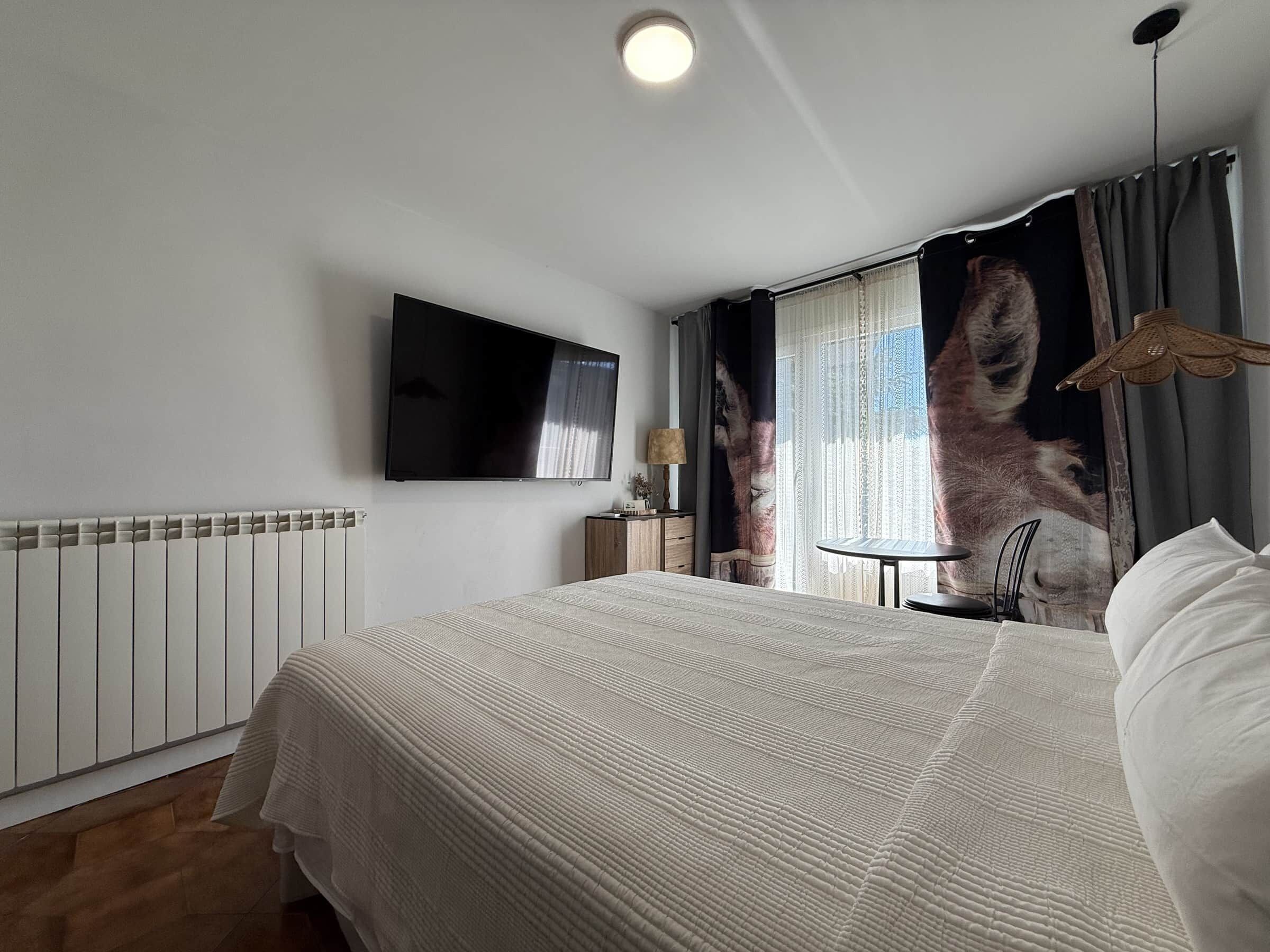 Habitación de hotel con cama, televisión de pantalla plana, mesa y cortinas.