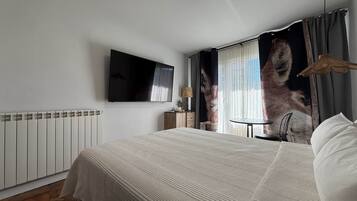 Habitación de hotel con cama, televisión de pantalla plana, mesa y cortinas.