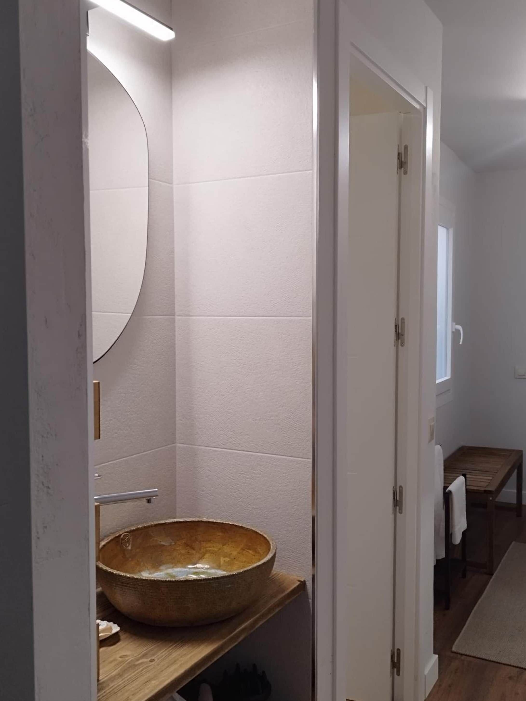 Un baño con un espejo redondo grande, un lavamanos de madera y un perchero para toallas.