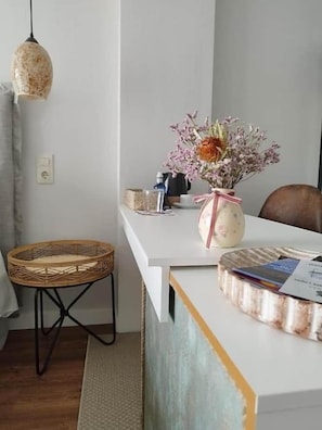A dining area with a white table, a wicker chair, a vase with flowers, and a hanging light fixture. - Ciervo del Castañar · El Cielo de Cebreros (Ávila) (Cebreros)