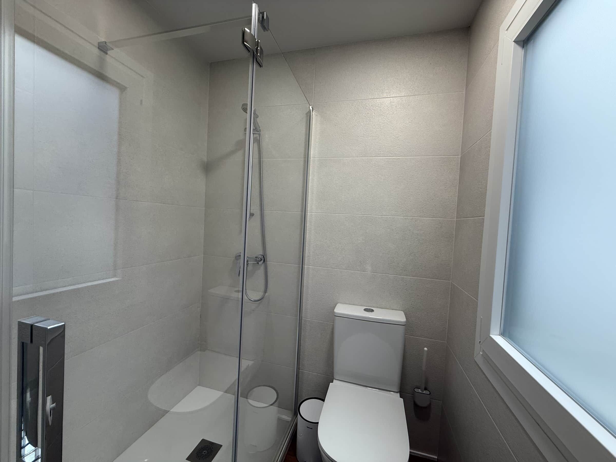 Un baño pequeño con ducha de vidrio, inodoro y ventana.