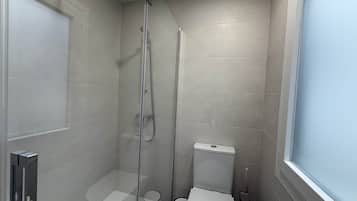 Un baño pequeño con ducha de vidrio, inodoro y ventana.