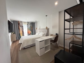 A modern bedroom with a bed, desk, chair, and a wardrobe with hanging space.
