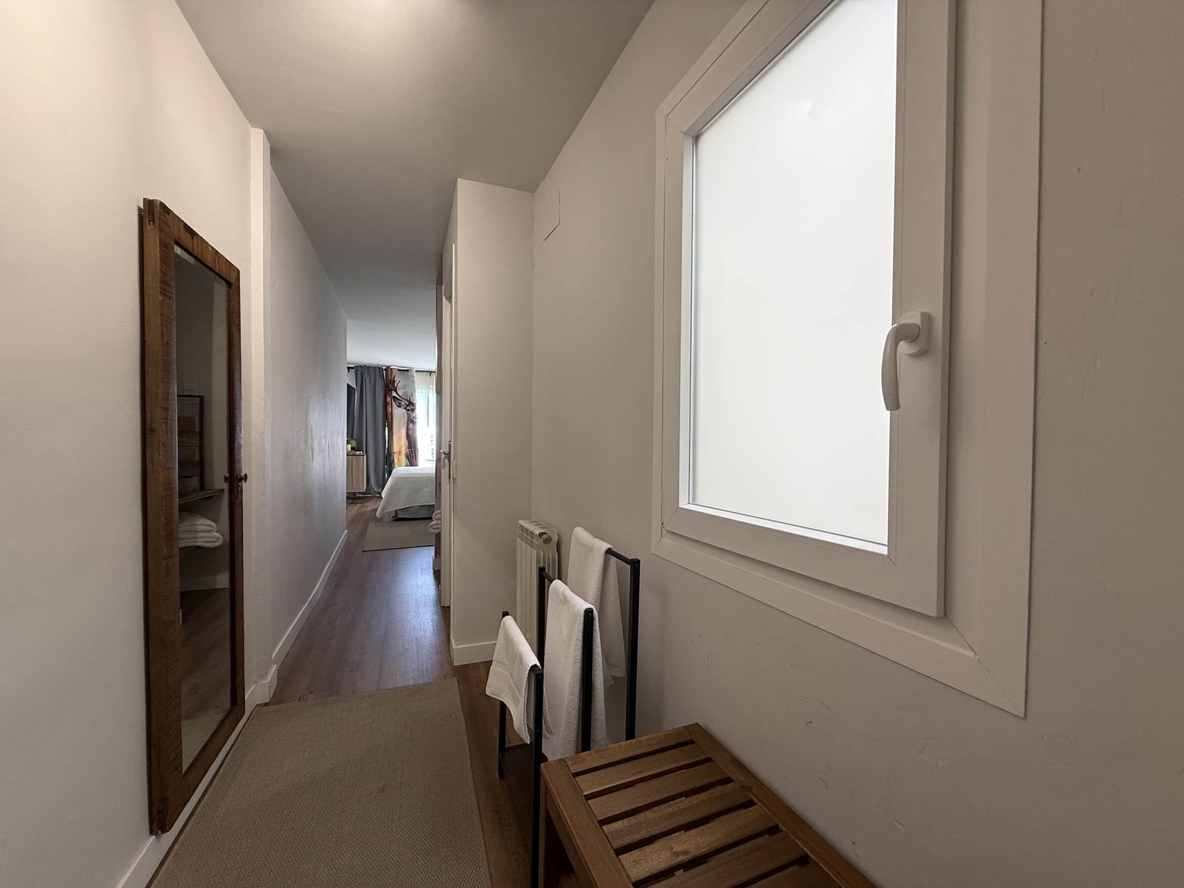 A narrow hallway with a wooden bench, a radiator, and a window with a white blind.