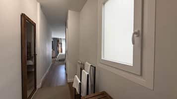 A narrow hallway with a wooden bench, a radiator, and a window with a white blind.