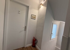 A hallway with a white door, a small window, and a red fire extinguisher.