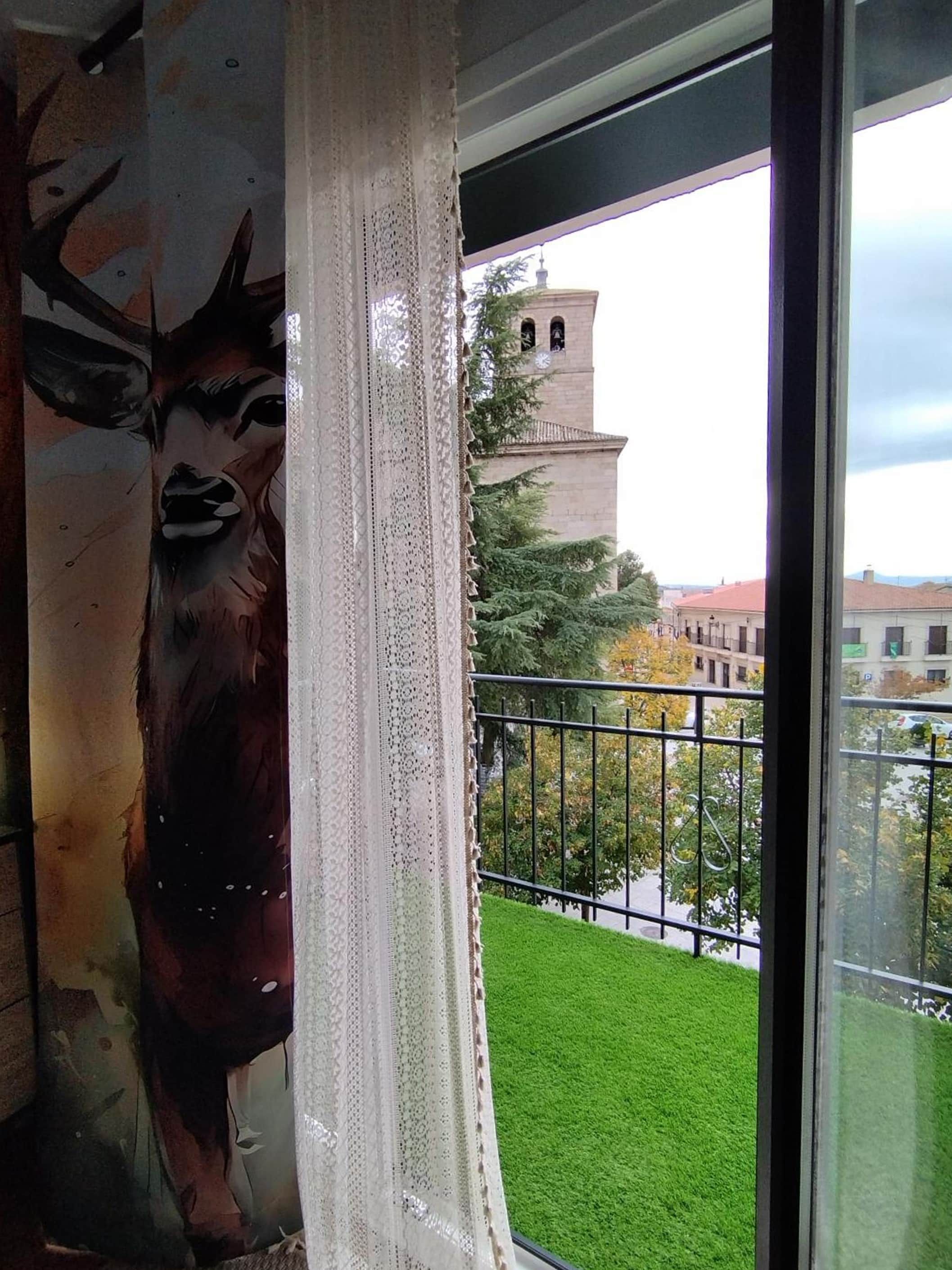 A room with a large window, a view of a building with a tower, and a green lawn outside.