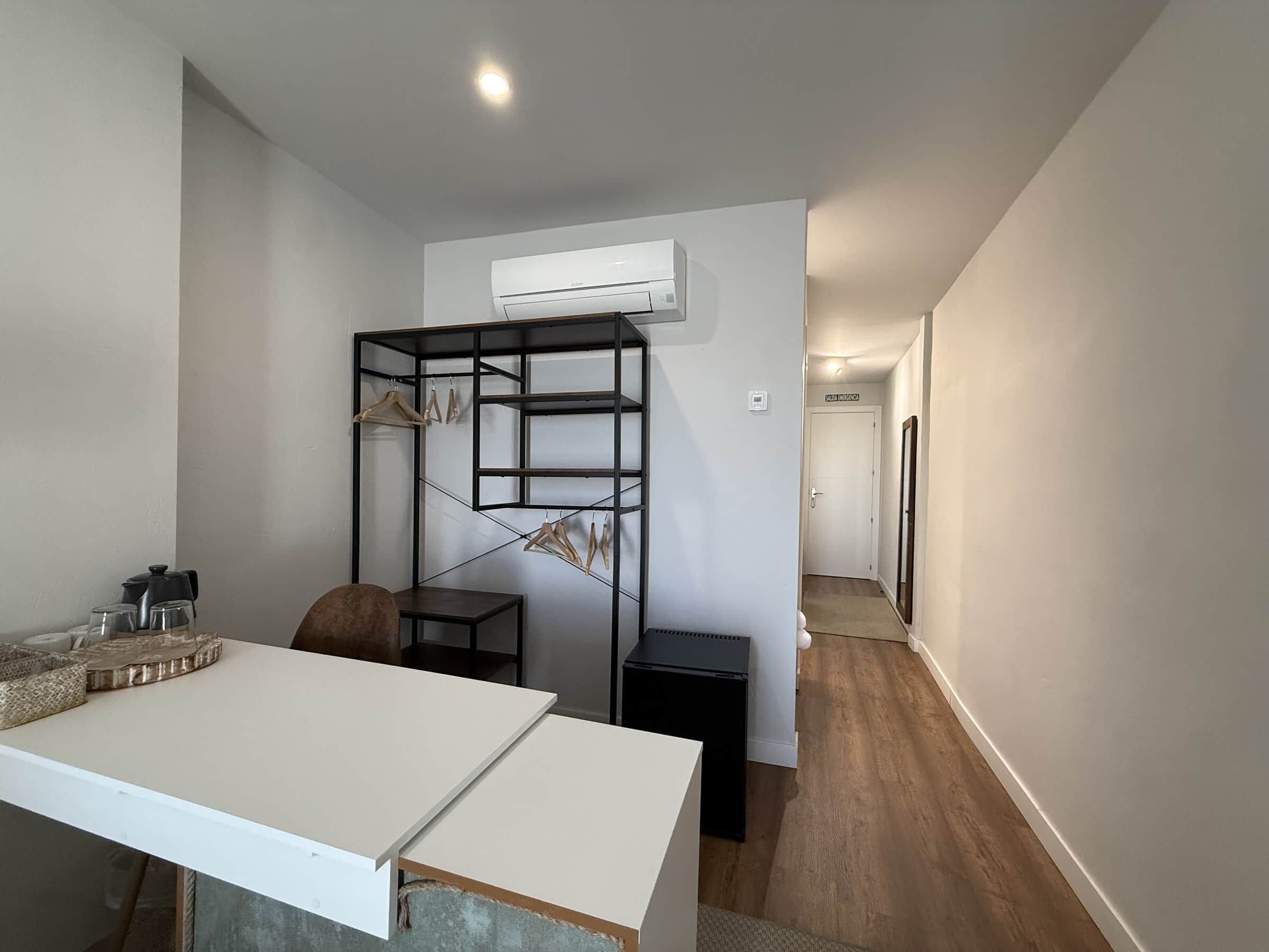 Una habitación moderna con un escritorio blanco, una estantería negra y un equipo de aire acondicionado blanco montado en la pared.