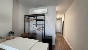 Una habitación moderna con un escritorio blanco, una estantería negra y un equipo de aire acondicionado blanco montado en la pared.
