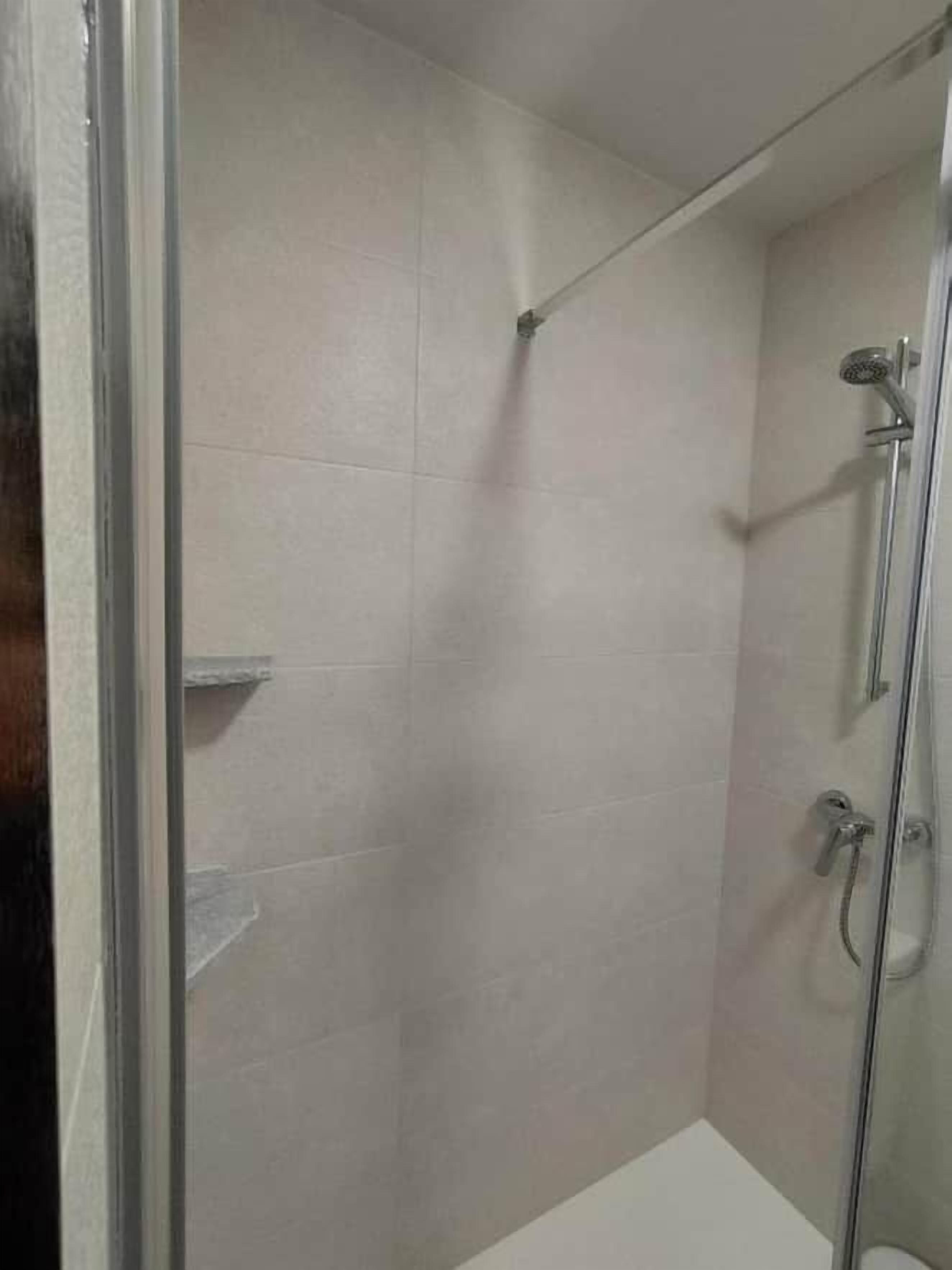 A glass-enclosed shower stall with a handheld showerhead and a wall-mounted faucet.