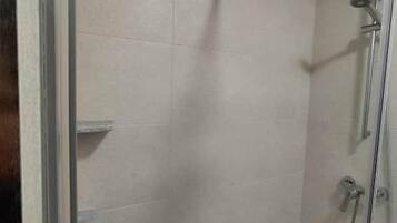 A glass-enclosed shower stall with a handheld showerhead and a wall-mounted faucet.