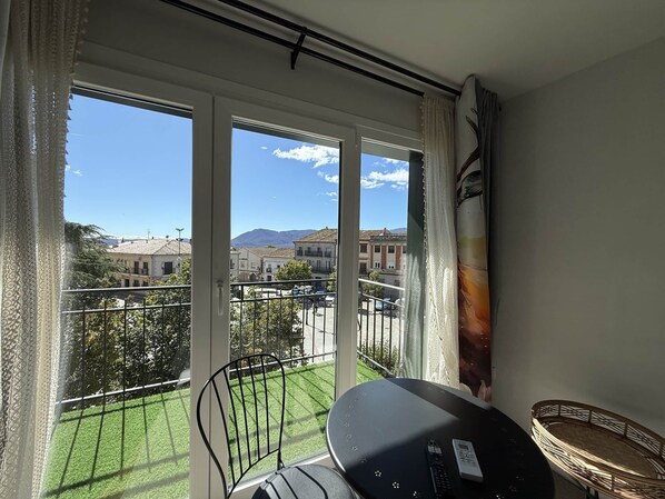 A balcony with a view of a town, a table with a chair, and a window with curtains.
