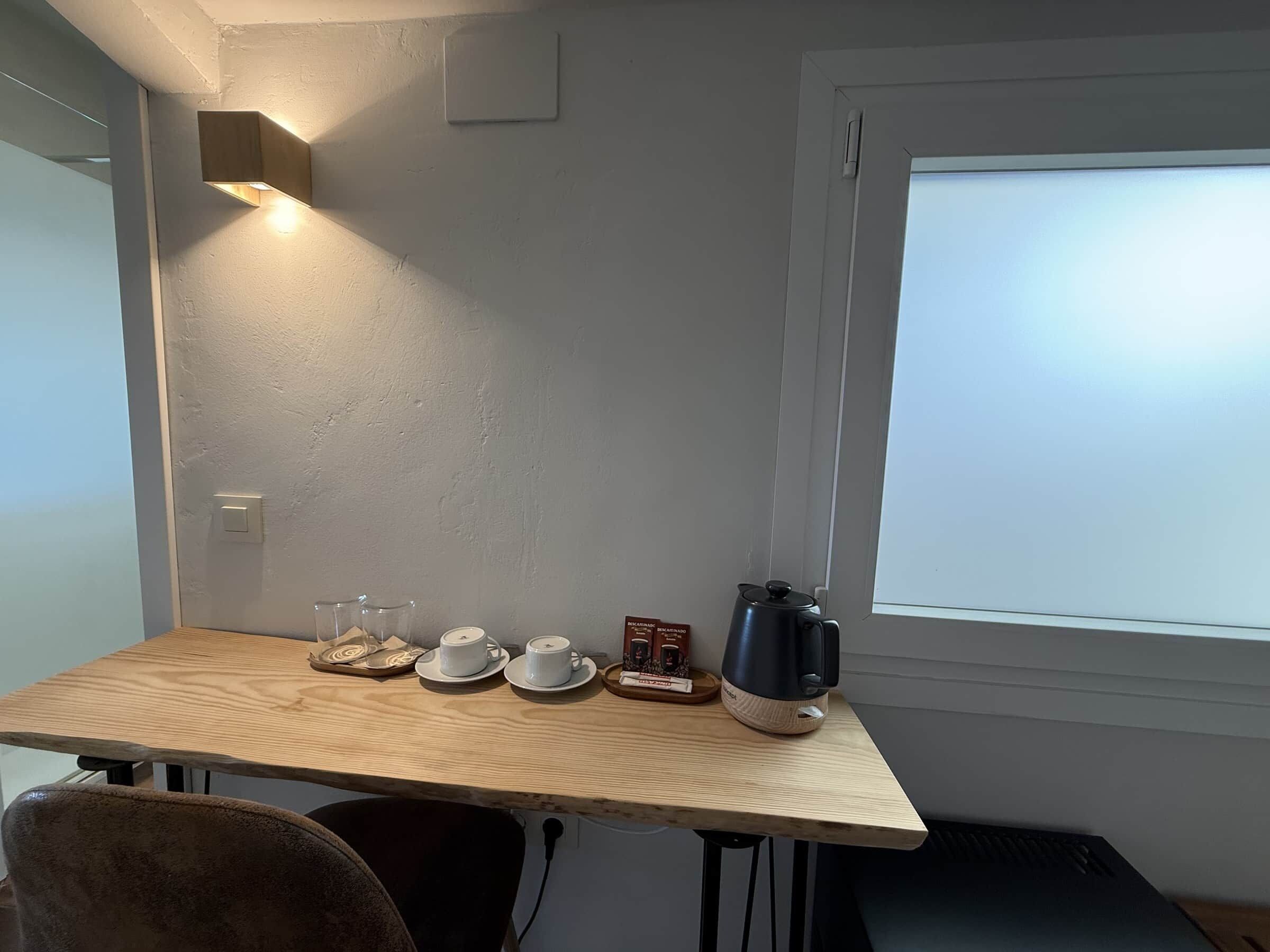 Une petite table en bois, avec une bouilloire, des tasses et une boîte de biscuits secs.