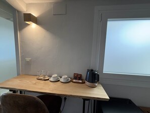 A small wooden table with a kettle, cups, and a box of biscotti.