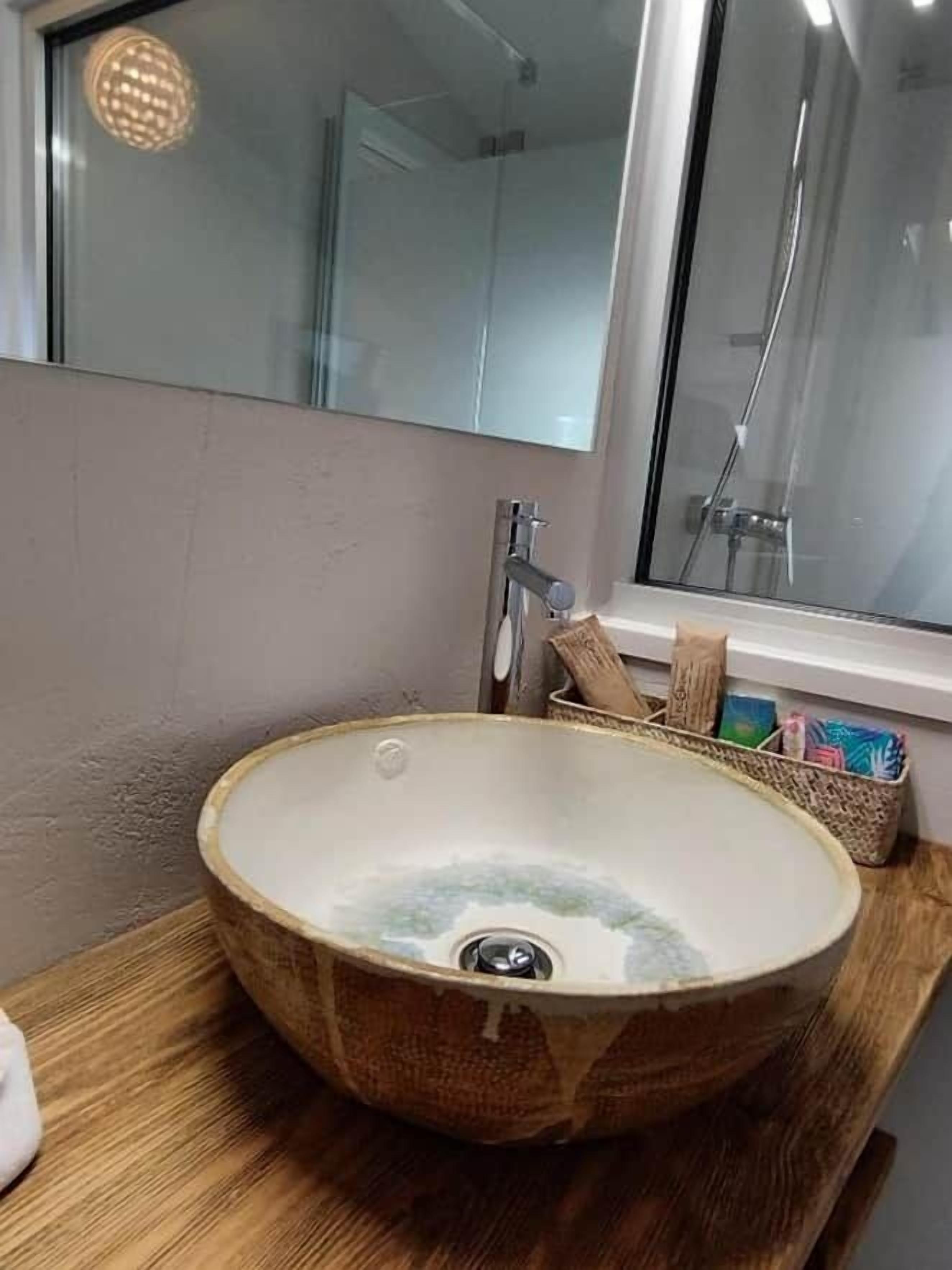 Un baño con un lavamanos de cerámica redondo, un espejo y una ventana.
