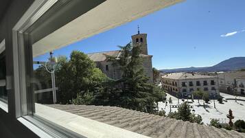Vista de una plaza de pueblo con una imponente torre de iglesia, rodeada de edificios y árboles.