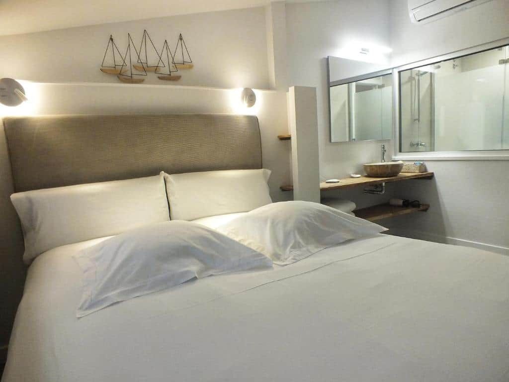 A bed with white linens, a headboard with built-in lighting, a bedside table with a mirror, and a wall-mounted shelf.