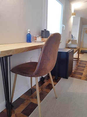 A modern kitchen with a wooden countertop, a brown upholstered chair, a black appliance, and a window providing natural light. - Tree of Life · The Sky of Cebreros (Ávila) (Cebreros)