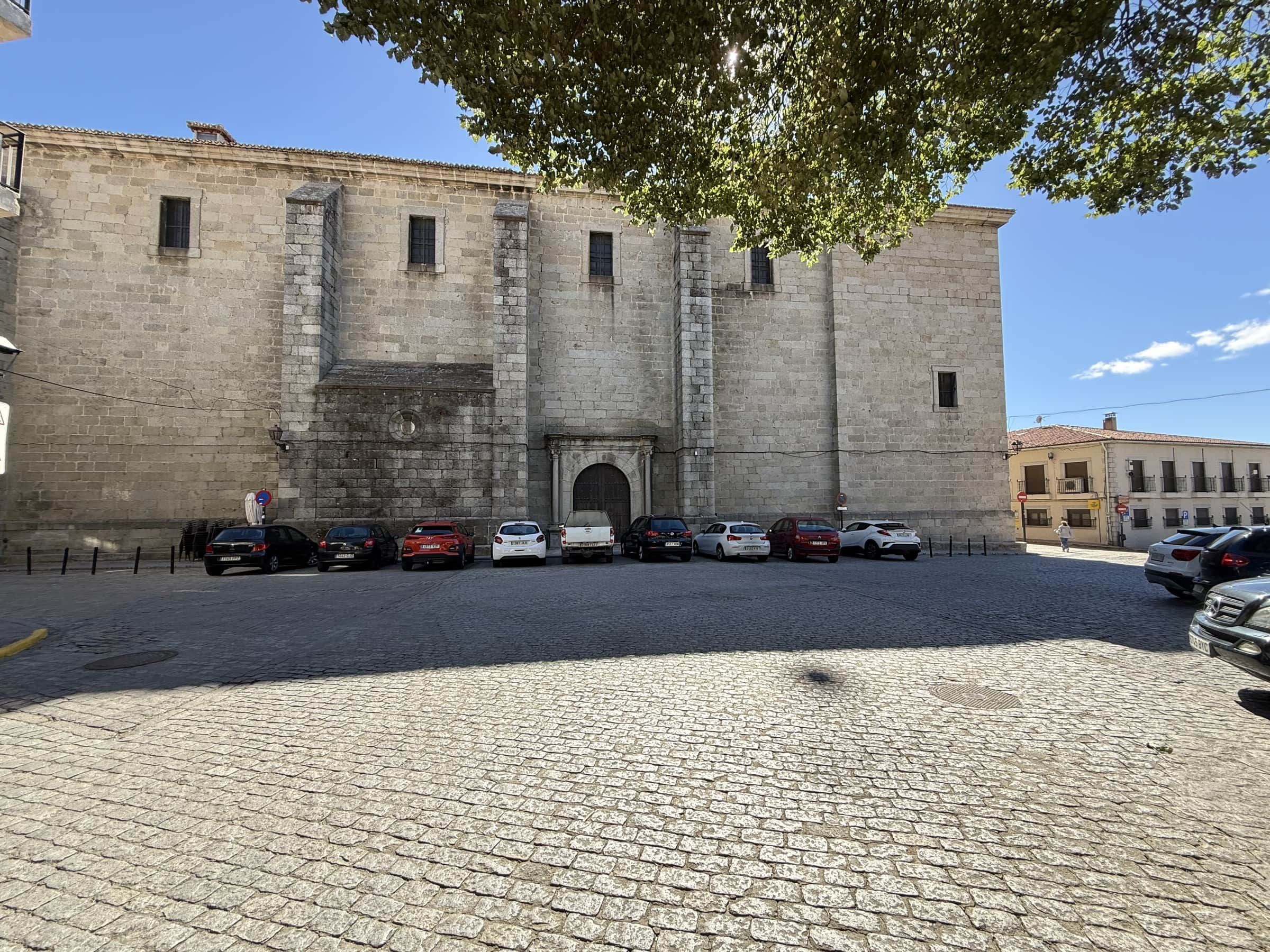Un edificio histórico de piedra con una entrada central, coches aparcados y una calle empedrada.