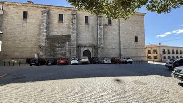 Un edificio histórico de piedra con una entrada central, coches aparcados y una calle empedrada.