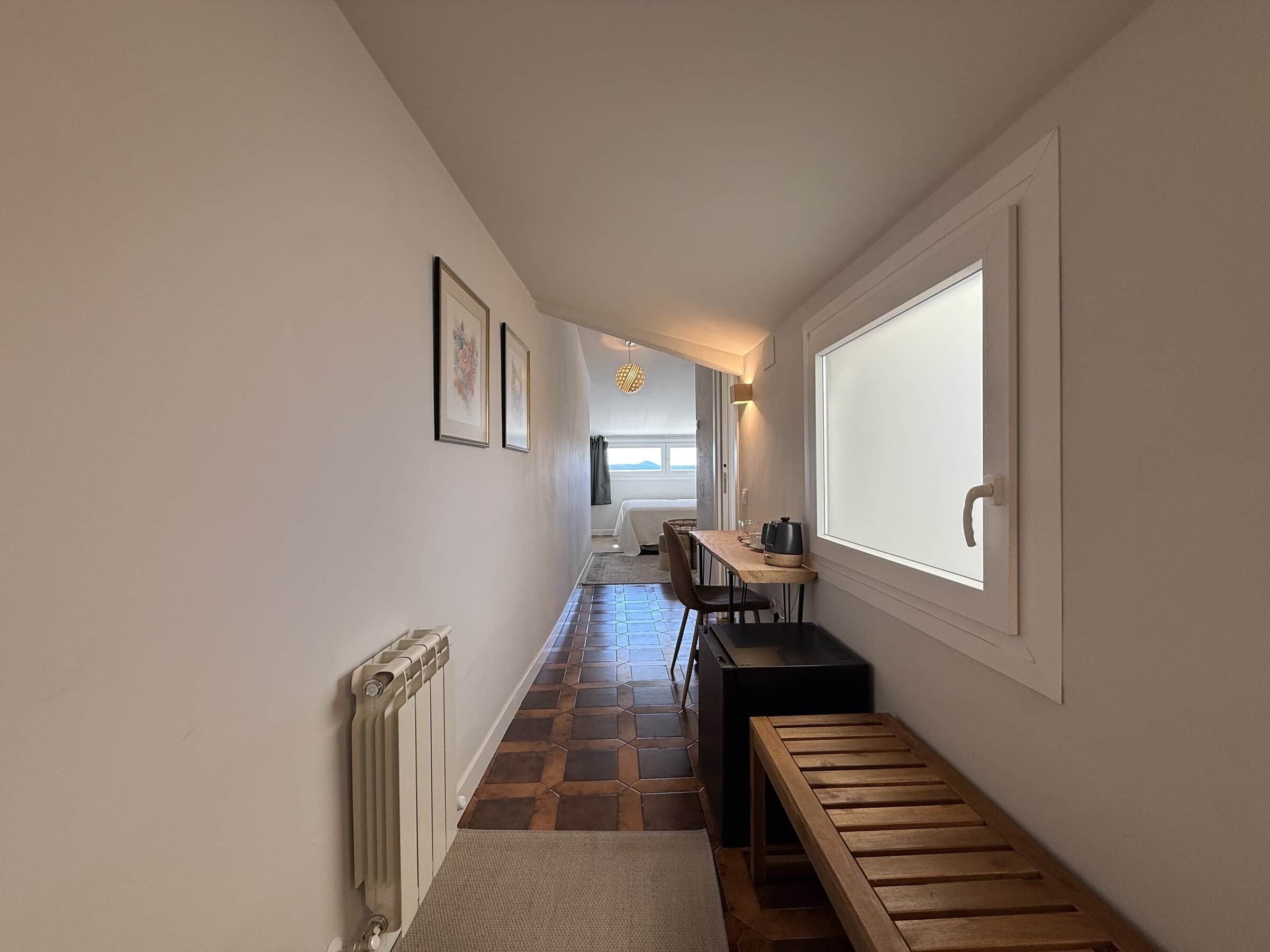 A hallway with a radiator, a bench, a table with a kettle, and framed pictures on the wall.