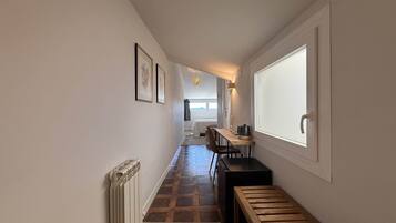 A hallway with a radiator, a bench, a table with a kettle, and framed pictures on the wall.
