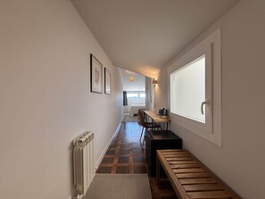 A hallway with a radiator, a bench, a table with a kettle, and framed pictures on the wall.