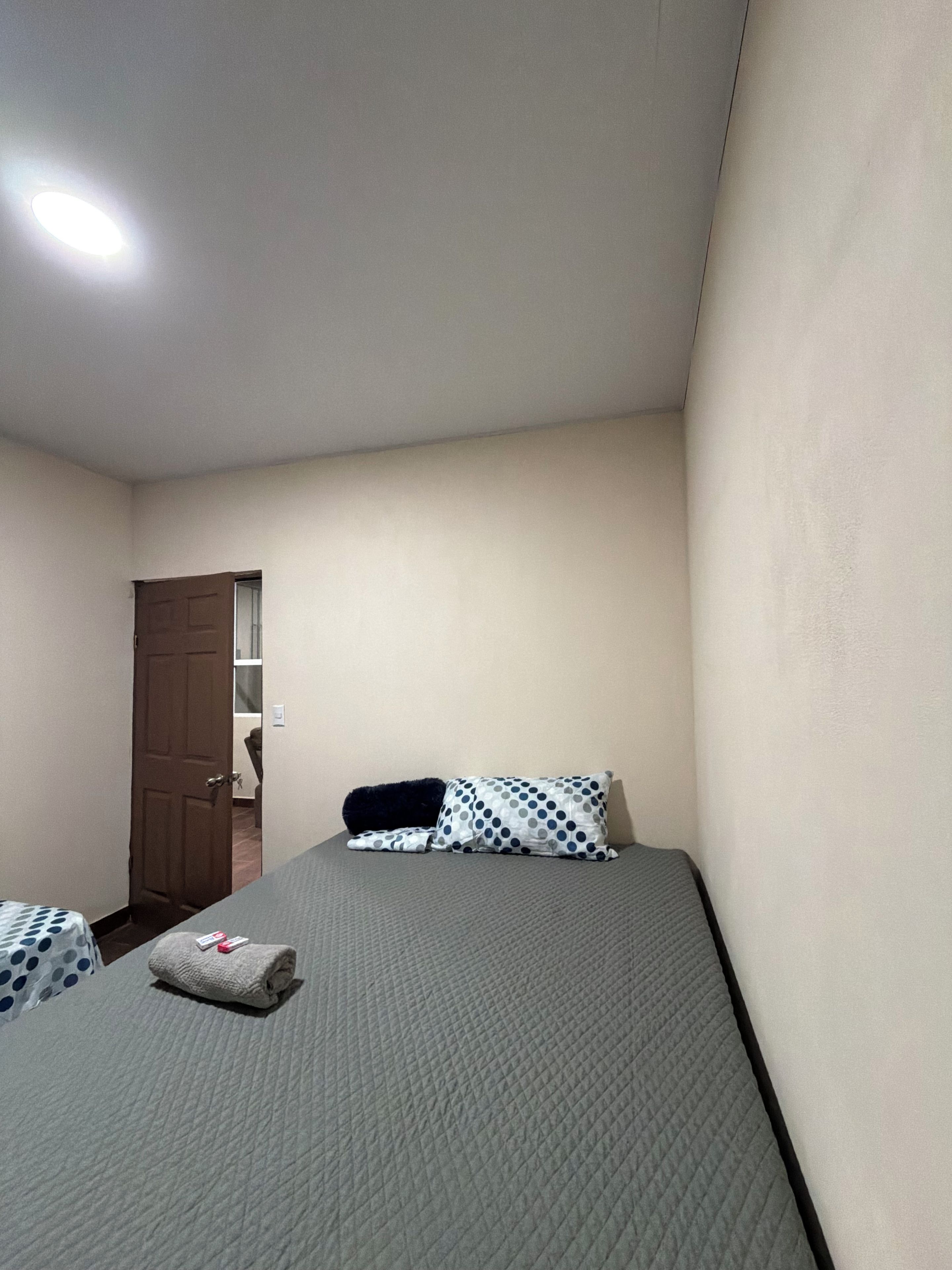 Une petite chambre avec un lit simple, une porte, une table de chevet et un lit recouvert d’une courtepointe.