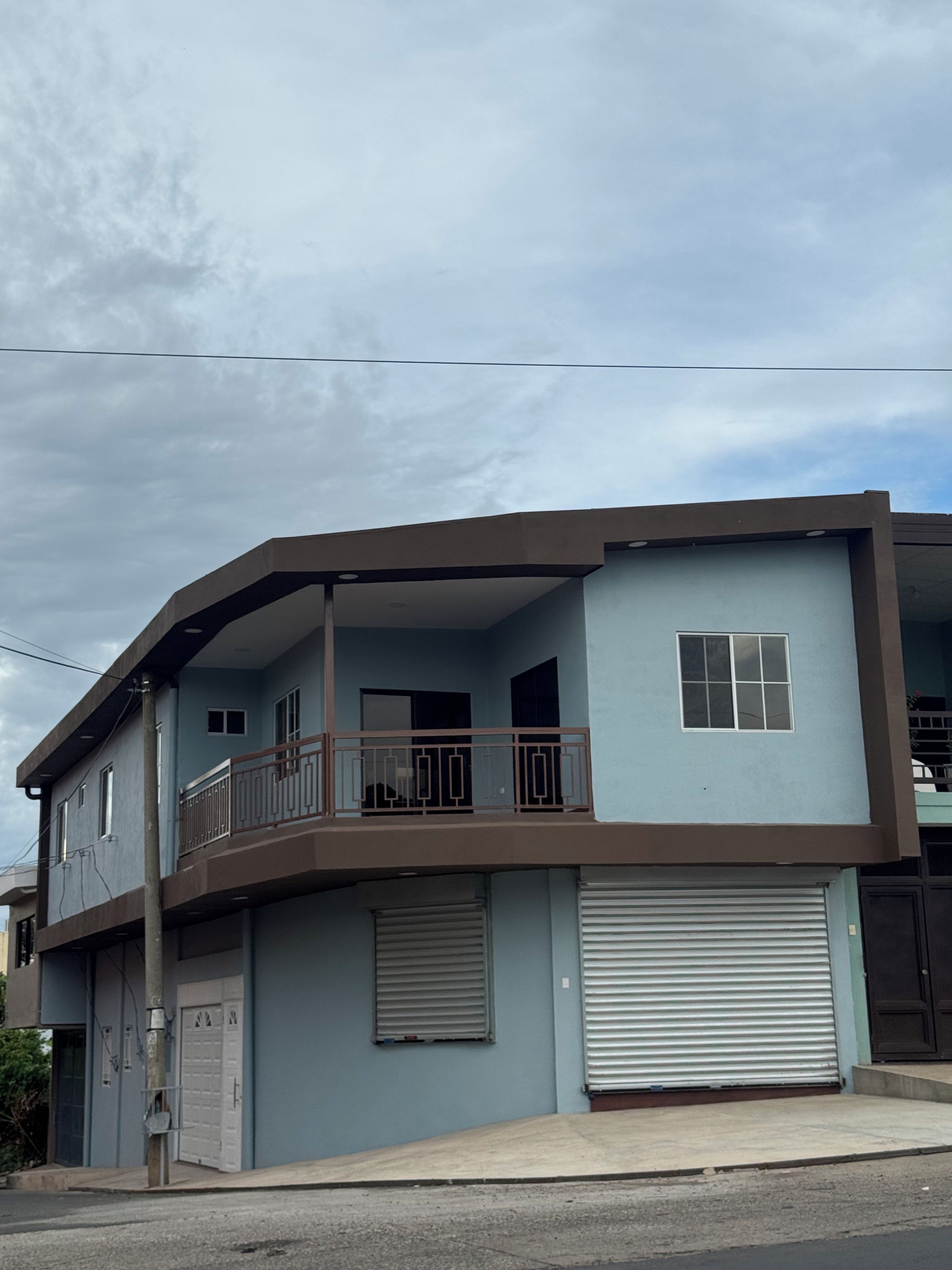 Un bâtiment à deux étages avec un balcon à l’étage supérieur, une porte de garage et un ciel dégagé en arrière-plan.