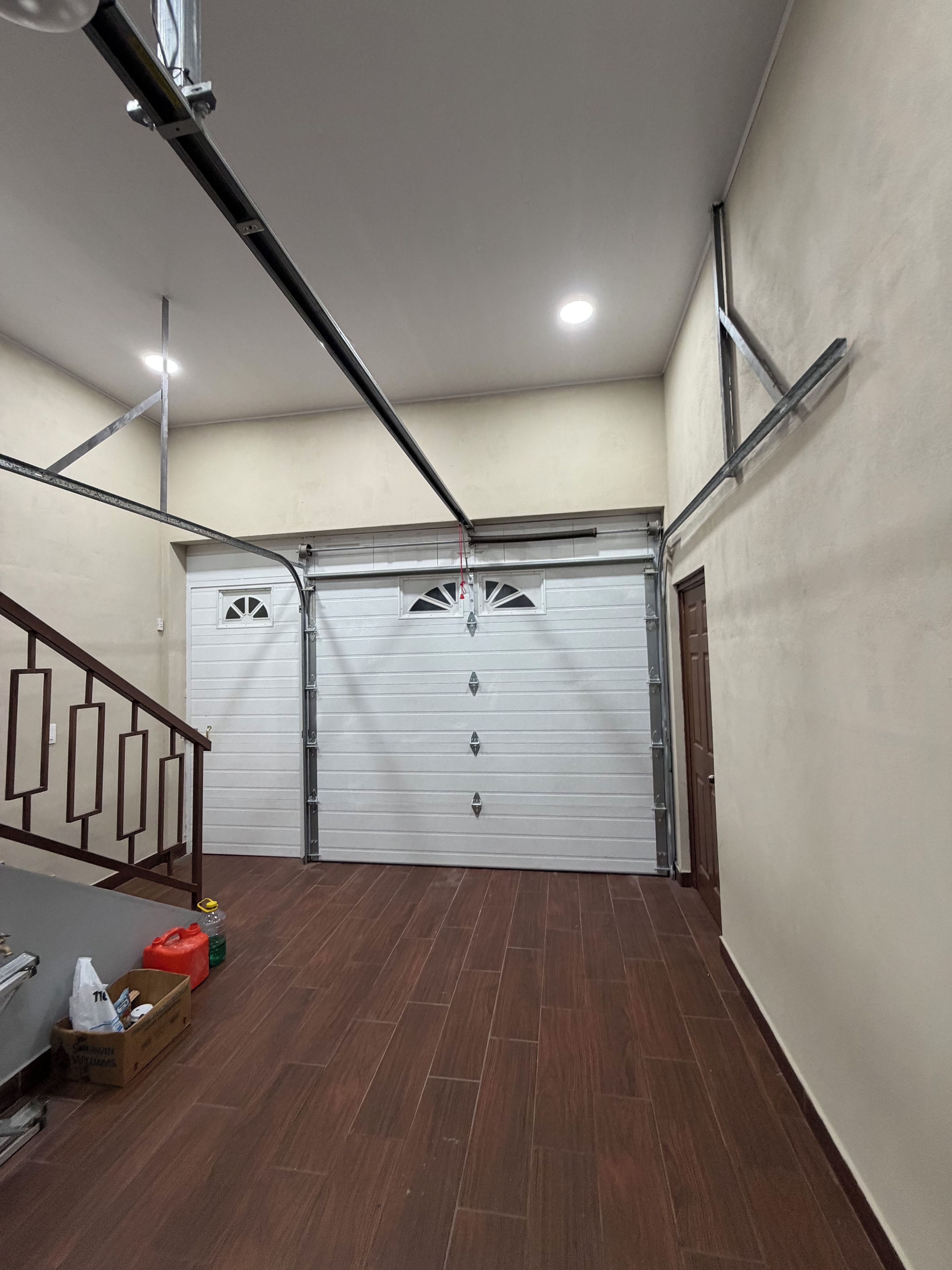 A garage with a white door, wooden floor, and a staircase with a geometric railing.