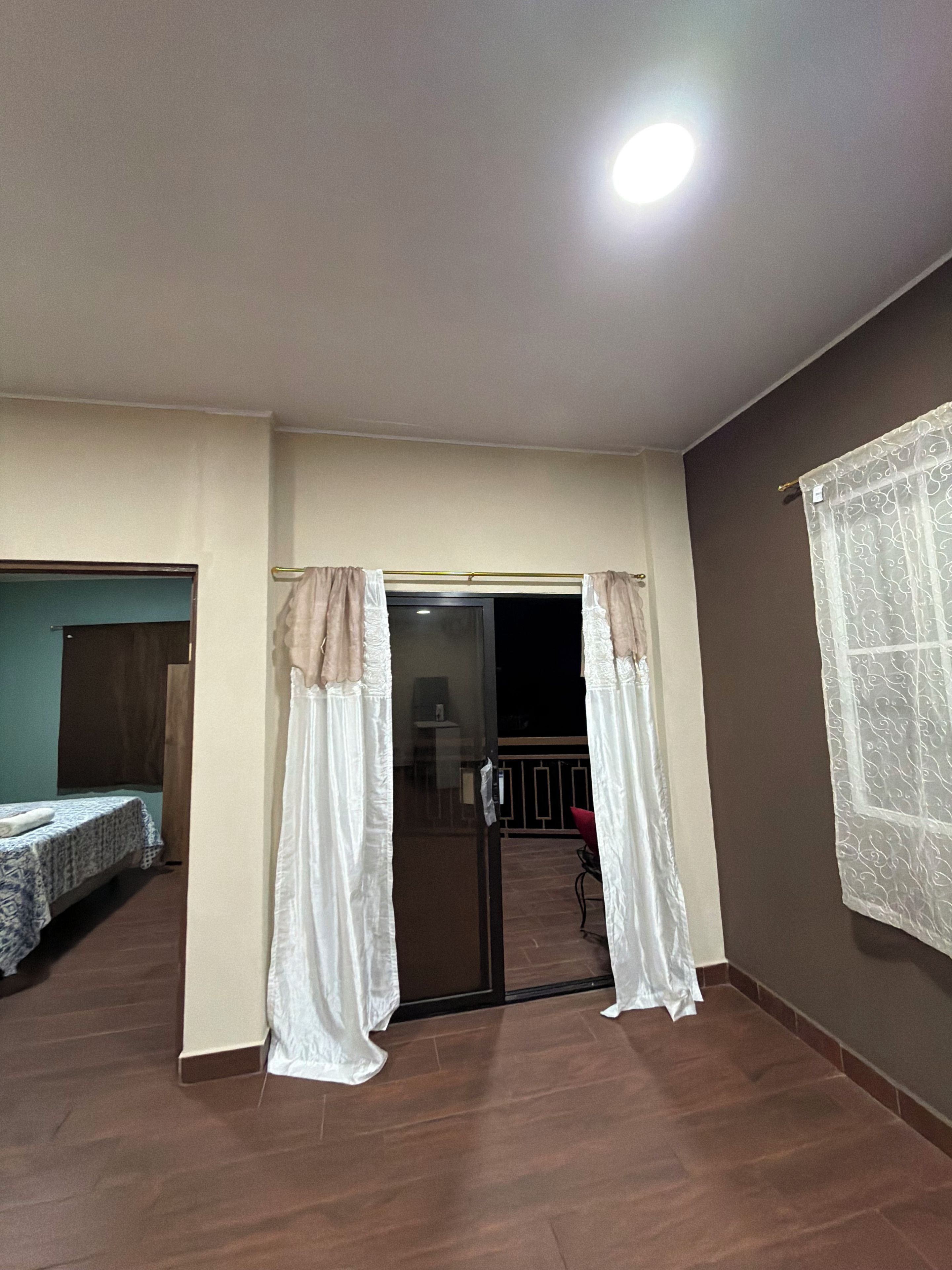 Ein Zimmer mit einem Bett, einer mit Vorhängen versehenen Tür, einem Balkon und Blick ins Freie.