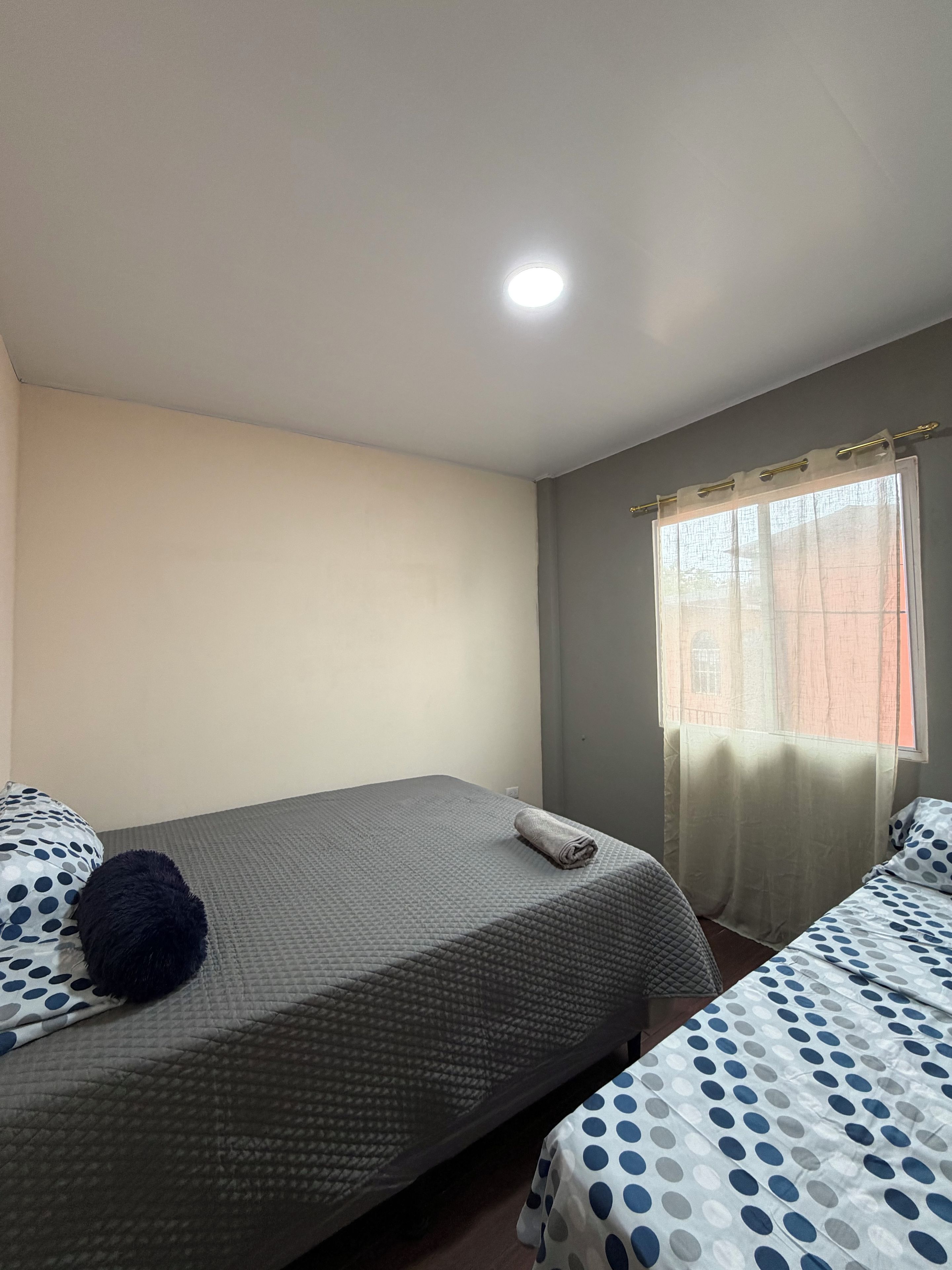A room with two beds, a window with curtains, and a ceiling light.